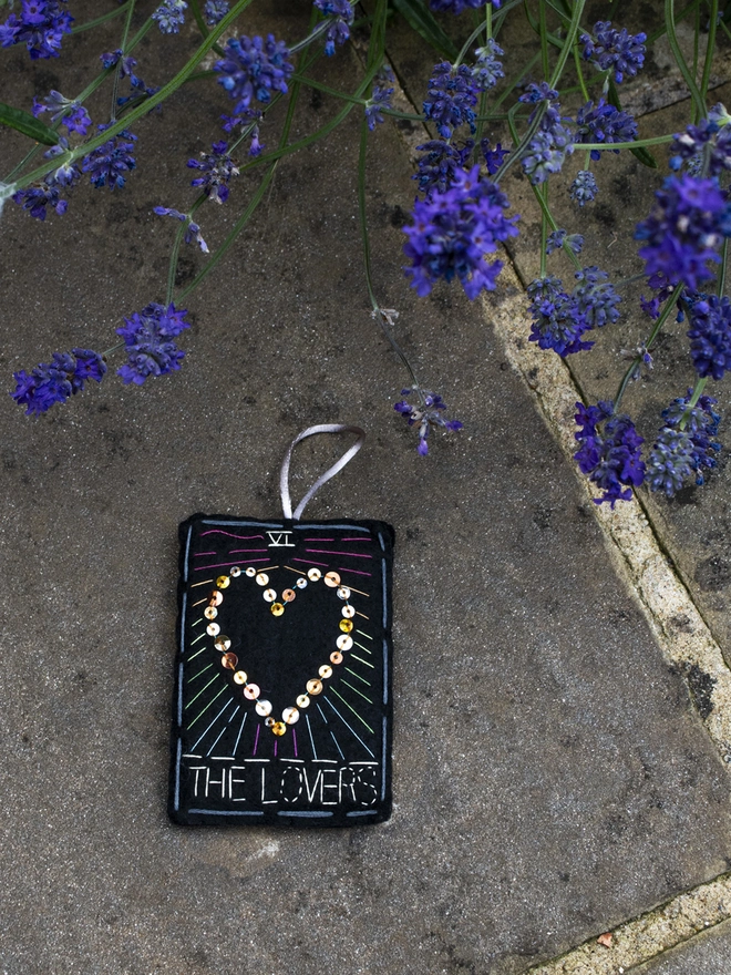 A handcrafted felt ornament with sequins and embroidery depicting "The Lovers" tarot card. Colourful embroidery with a heart shape. 