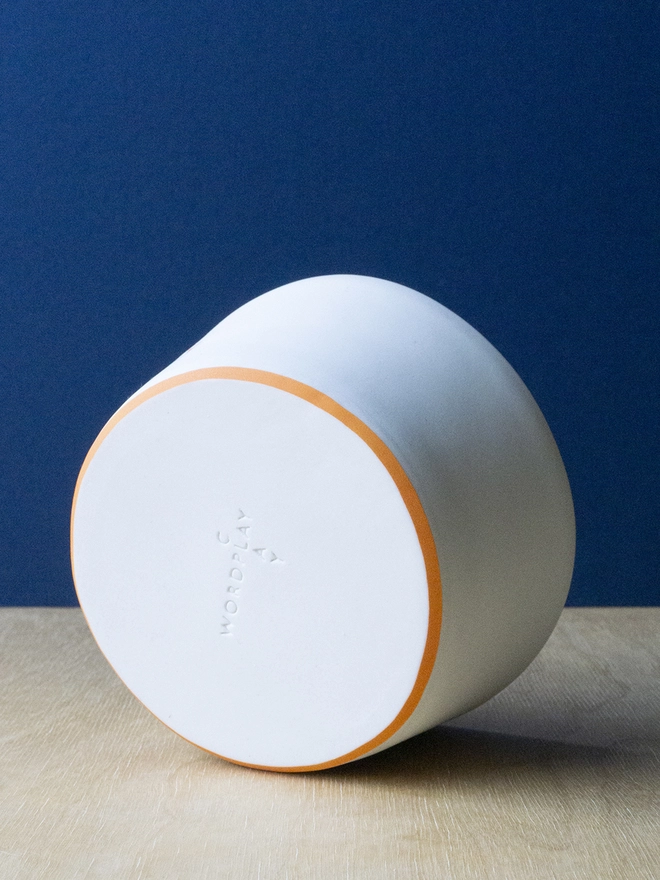 Ceramic porcelain pudding bowl with orange rim and Wordplay Clay stamped into the base.