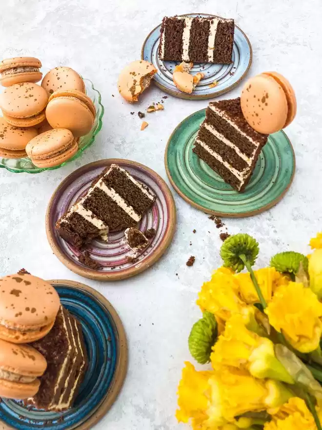 several pieces of carrot cake and macarons on a table with daffodil flowers