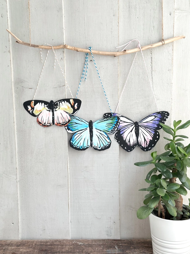 3 Hand Painted Butterflies. Set Of Linocut Wall Hangings displayed on a stick. Colours are purple and peach and teal  