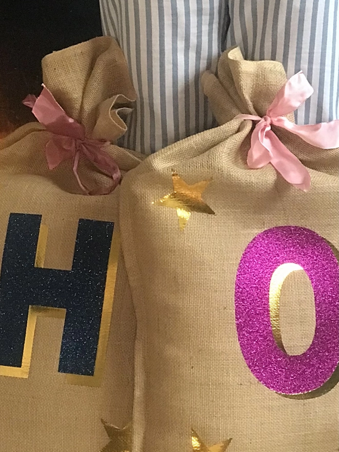personalised 3D christmas sacks in navy glitter and pink glitter next to elf's legs