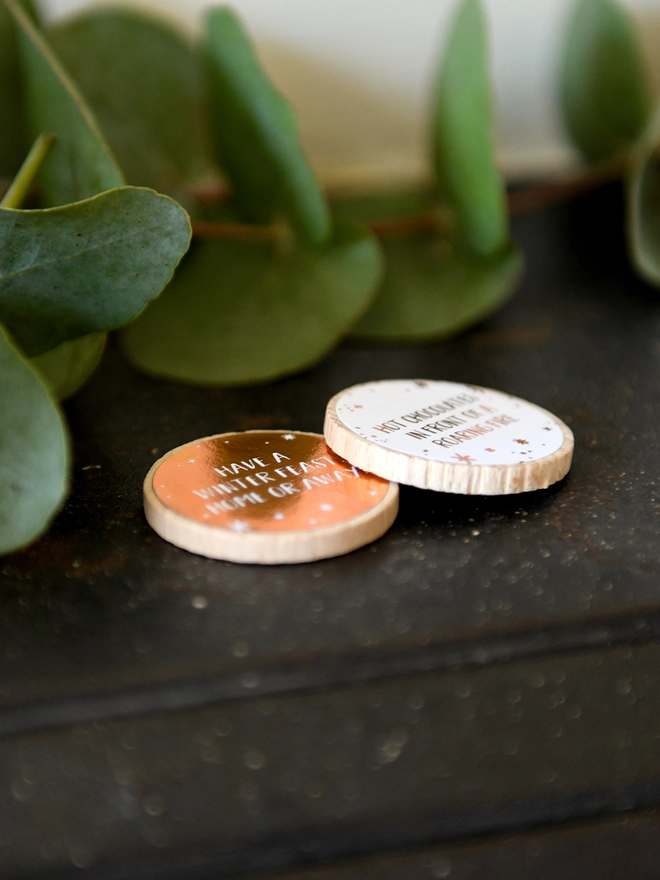 Two wooden tokens with copper foiled tokens lay on black mantlepiece. Each token has a different date night idea on.