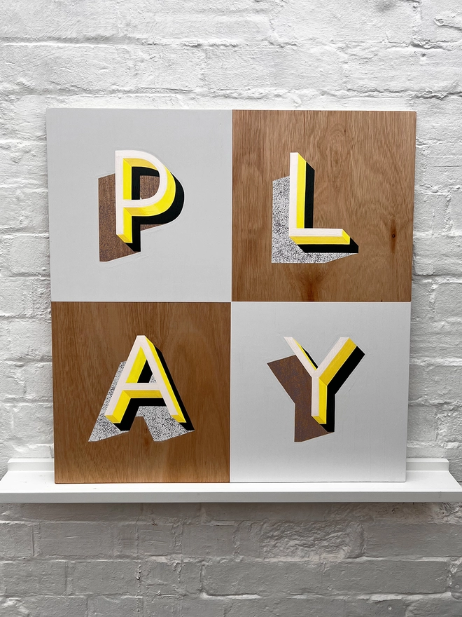 PLAY hand painted sign in neon yellow, lilac and grey, against a white brick wall, straight on. 