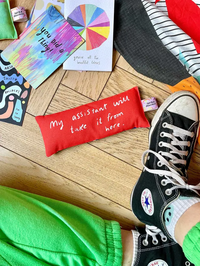 Bright red lavender eye pillow on a wooden floor amongst Nicola's brightly coloured products