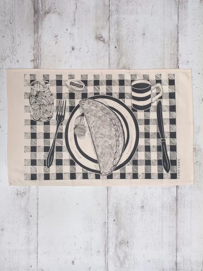 Picture of a tea towel with an image of a Cornish pasty on a plate, taken from an original lino print