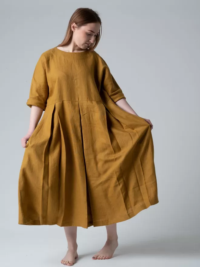 Midi length linen dress in golden colour. Loose and comfy fit with pleated skirt. Studio front view.