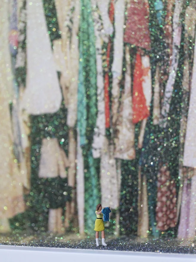 A tiny woman holds up a sparkling blue item of clothing set against a sparkling interior of an overflowing wardrobe (close up)