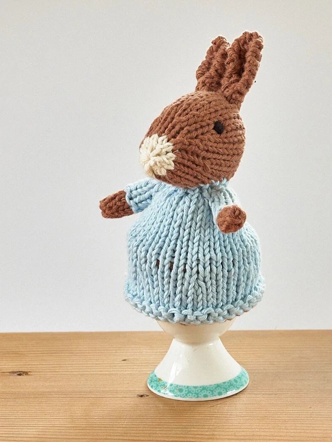 Egg Cosy Rabbits Easter Table Decoration, an Easter cosy sitting on a wooden surface. 