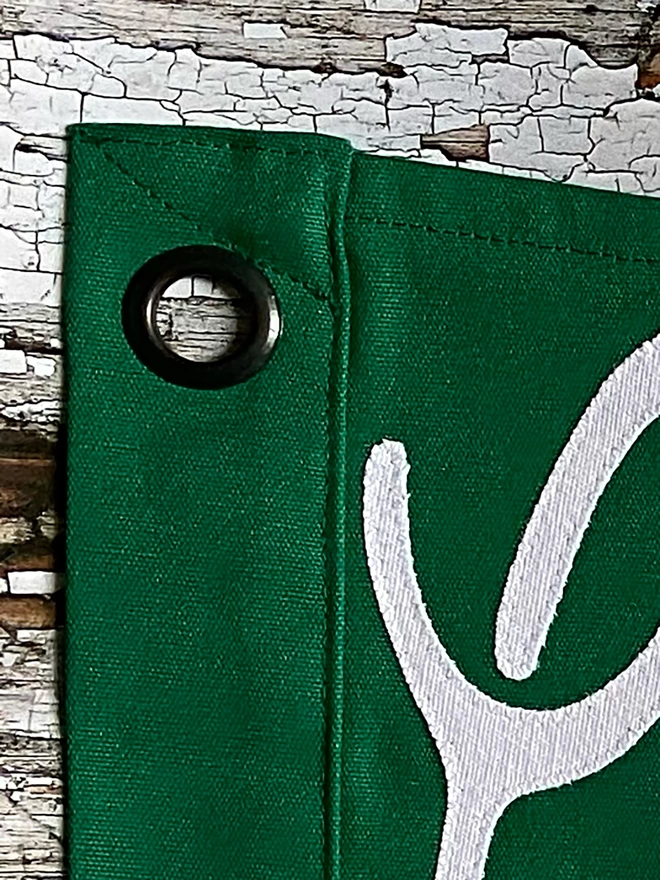 Detail of a green Coffee before Gin pennant flag. It shows one of the hanging eyelets.