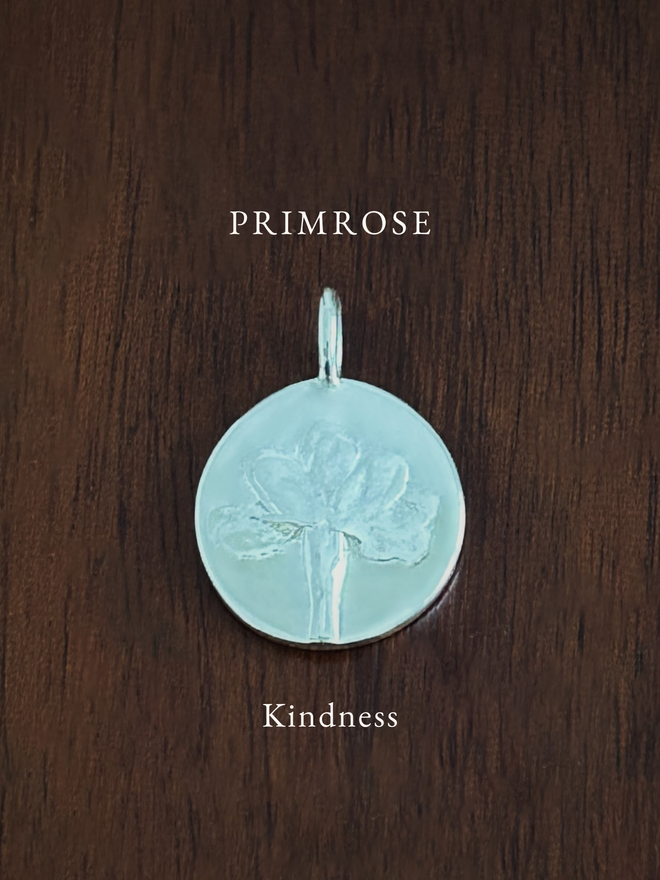 Sterling Silver Primrose Coin Charm on a dark background with the language of flowers meaning, kindness