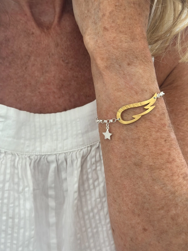 model wears a personalised gold wing charm on a silver belcher chain bracelet with a silver mini star