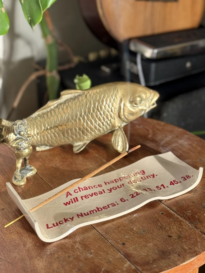 Fortune Incense Holder, an incense holder sitting on a wooden surface. It is joined by a fish sculpture. 