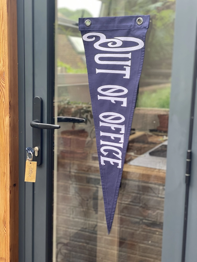 A navy out of office pennant flag hanging on an office door