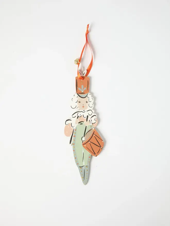Little Drummer Tree Dancer. wooden hanging little drummer decoration with a curly white wig, terracotta hat and drum, sage green uniform, orange ribbon with a jingle bell, on a white background