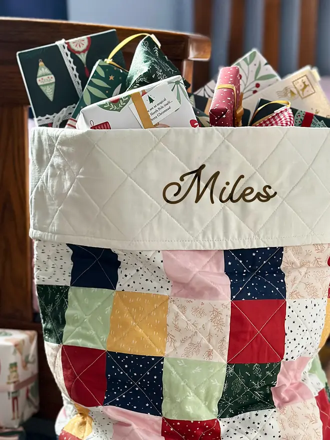 A tiny Christmas wish card is tucked into the ribbon on a wrapped gift at the top of a patchwork Christmas stocking.