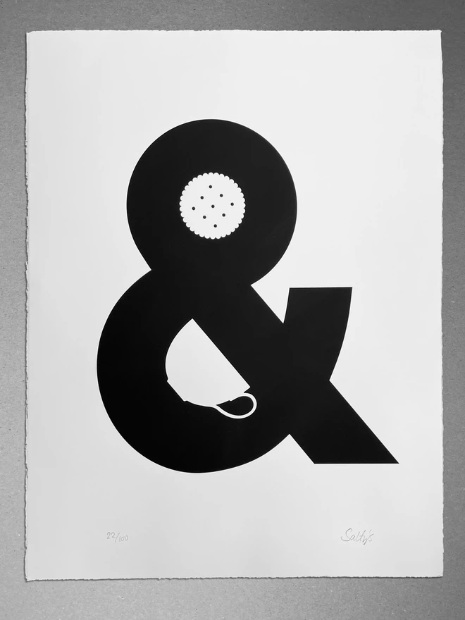  A monochrome print of an ampersand with a china cup and a biscuit made out of the negative space. It reads visually as Tea and Biscuits.