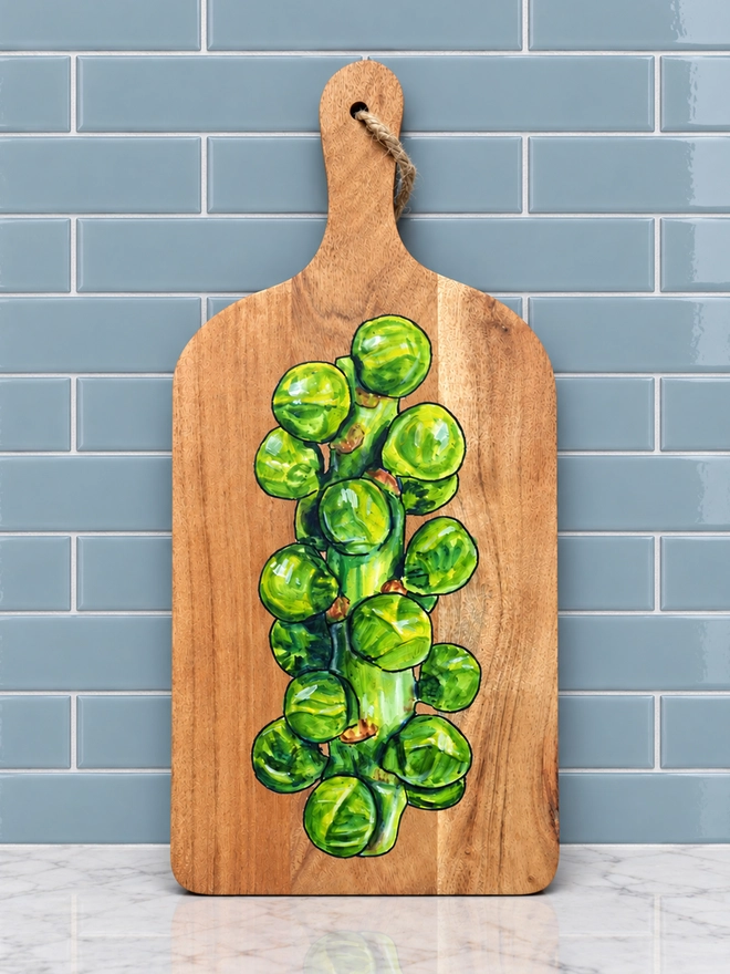 A wooden serving board with a handpainted design of a stalk of Brussels sprouts