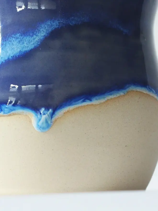 Zoomed in “Sea, please” ceramic mug with a glossy blue top glaze and natural ceramic bottom, placed against a plain white background.