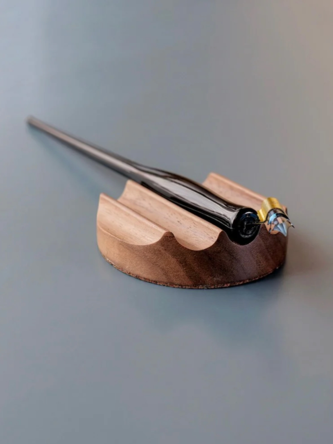 Tani Wooden Pen Rest. The rest, in Walnut, is shown in use with a pen.
