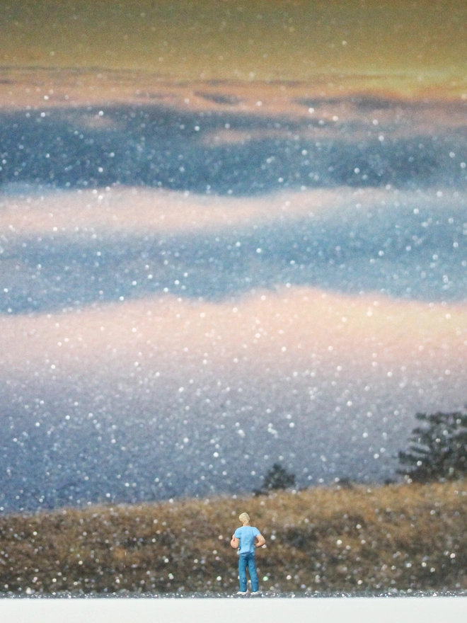 TIny figure of a young man looking out from a hill overlooking the beautiful sunset through clouds (close up)