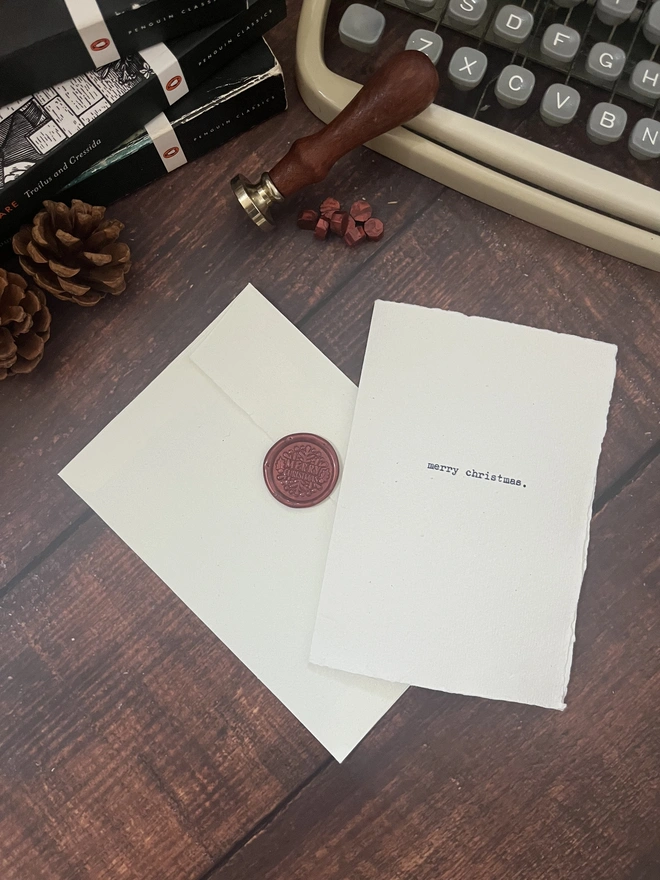 handmade a6 christmas card typewritten with an antique typewriter with the words merry christmas onto cotton rag deckle paper. with a matching c6 cotton rag envelope and a red christmas wax seal stamp 