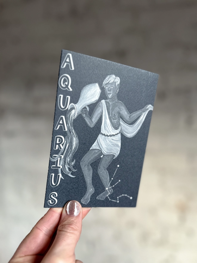 a greetings card featuring a greyscale illustration of a zodiac style water bearer with the text “AQUARIUS”