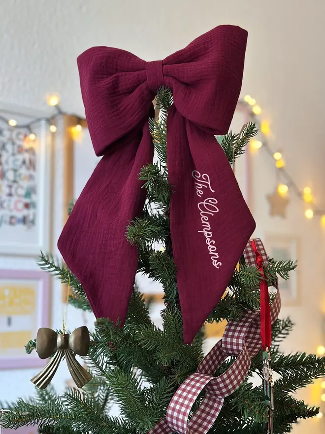 A handmade burgundy Christmas bow tree topper sits at the top of a decorated Christmas tree.