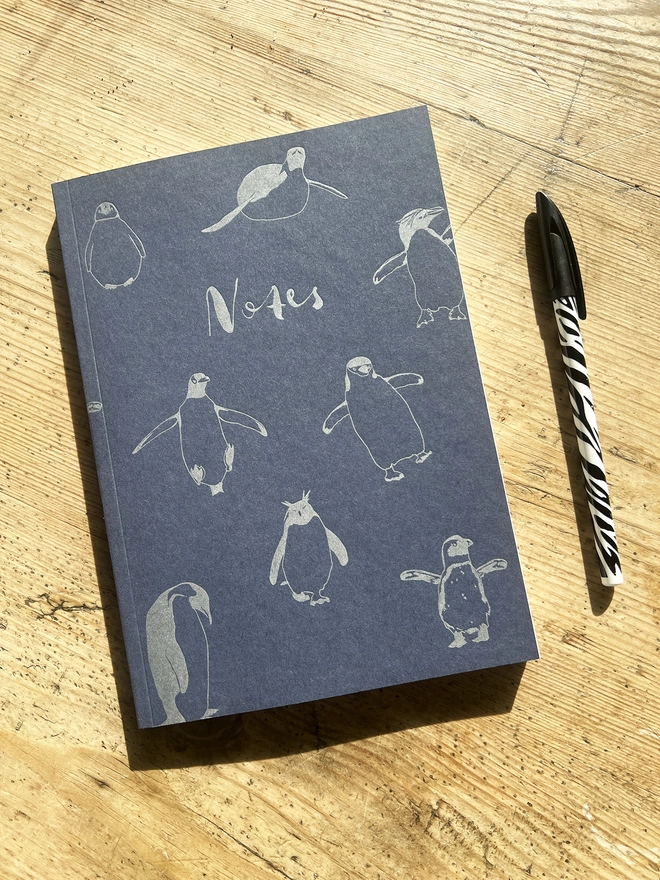 Front of the multi penguin notebook with a pen next to it.