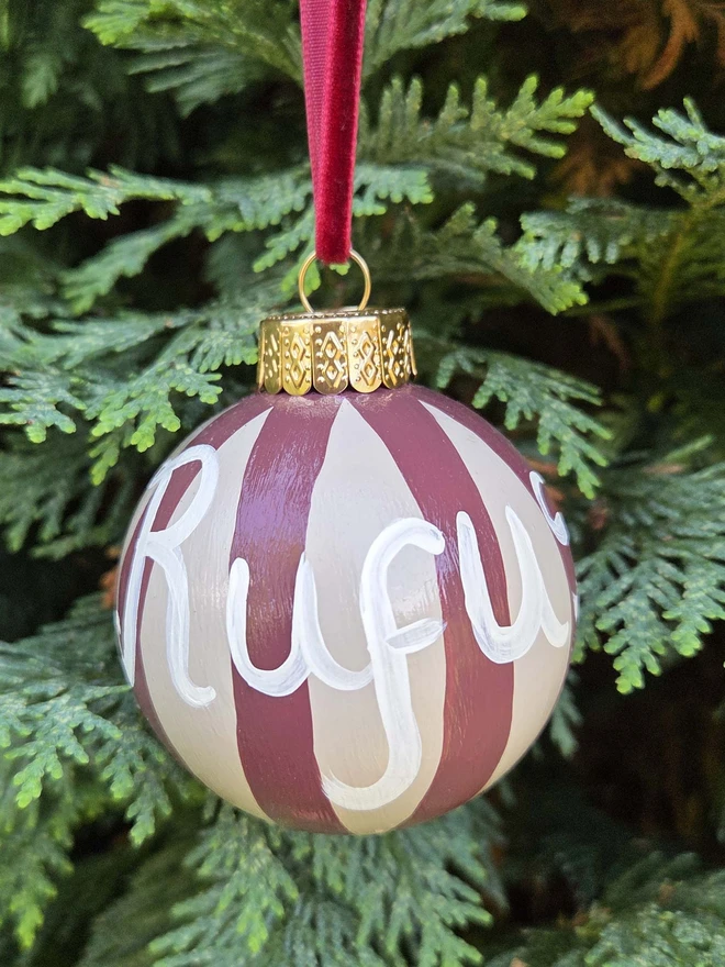 hand painted beige and brown stripe bauble with name personalisation, hanging on a christmas tree