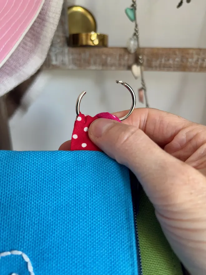 Hand holding the keyring on a blue coin purse, showing how the hinged ring opens easily.