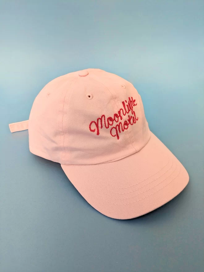 Powder Pink adult cap with Red embroidery reading 'Moonlight Motel' on a blue background