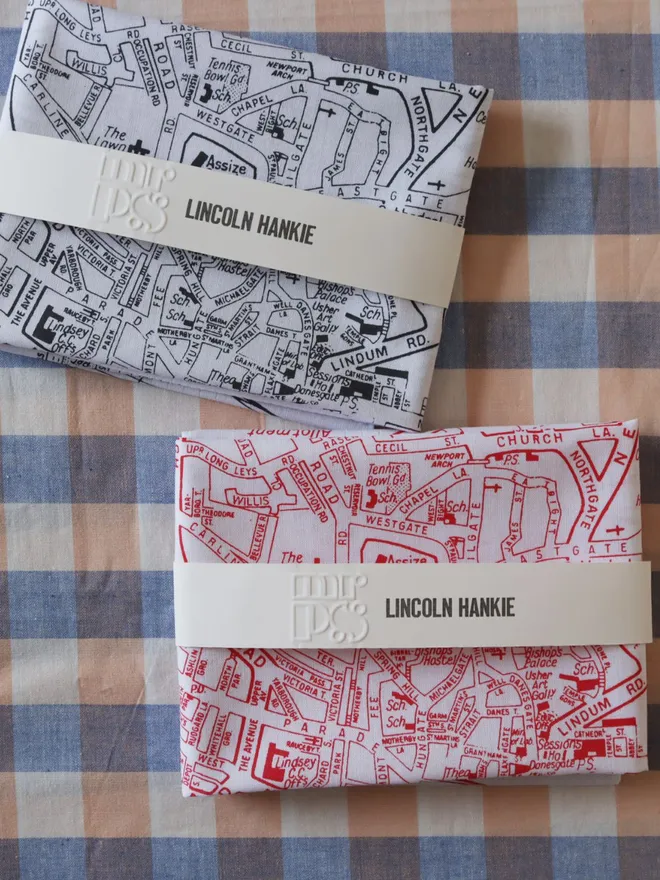 Two folded Mr.PS Lincoln map hankies, one in grey, and one in red, shown on a gingham tablecloth