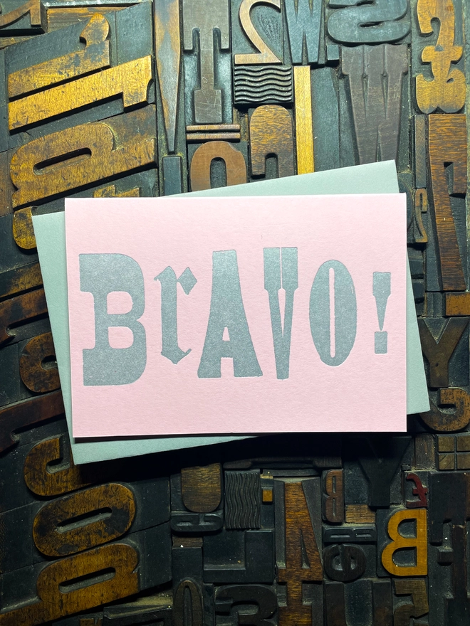 A congratulatory letterpress candy pink card featuring the deep impression word "BRAVO!"; in bold metallic gold letters with a set of colourful envelopes. Perfect for exam results and graduations and other celebrations and milestones.