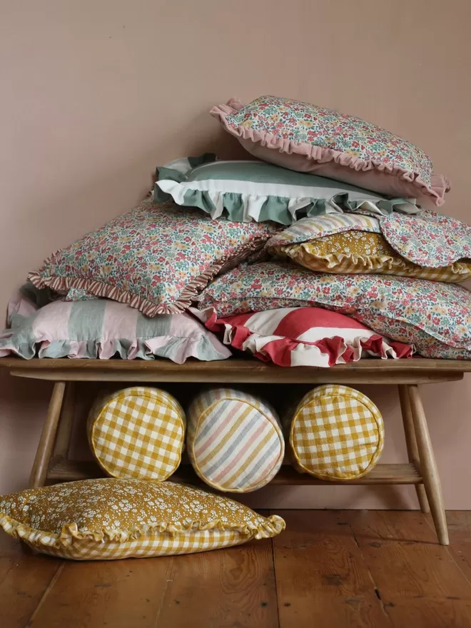 Ruffle Cushion in 'Gelato' cushion amongst a pile of other cushions on a bench