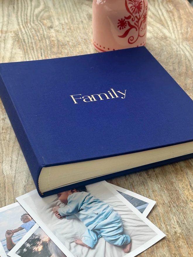 on a wooden table there is navy blue album which has been printed with the word Family on the front.