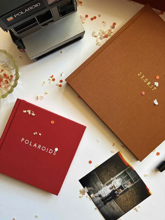 Confetti littered table with two instant photo guestbooks by Keep Collect with Polaroid camera and photograph
