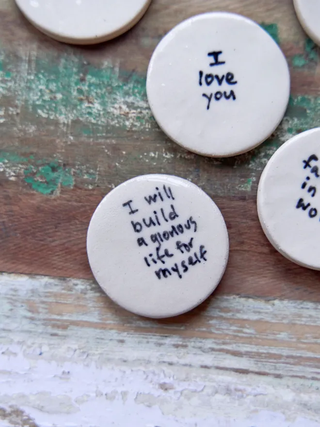 Small ceramic love token. Ceramic love tokens with phrases written on them in black on a wooden surface