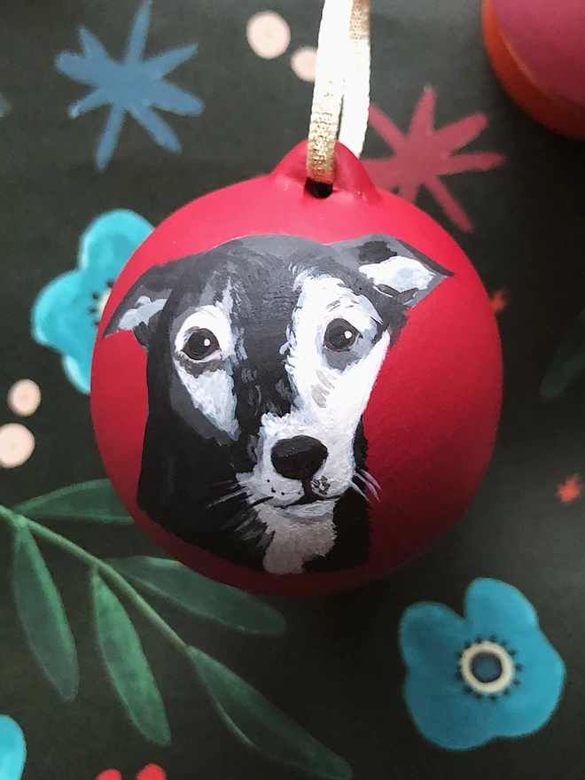 A black dog with greying hair at the eyebrows and muzzle painted on to a red Christmas ornament