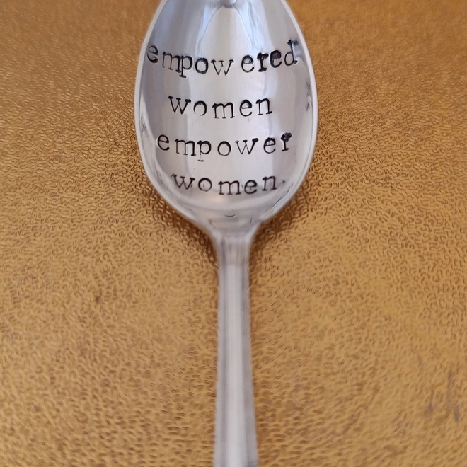 Teaspoon on gold background stamped with empowered women empower women