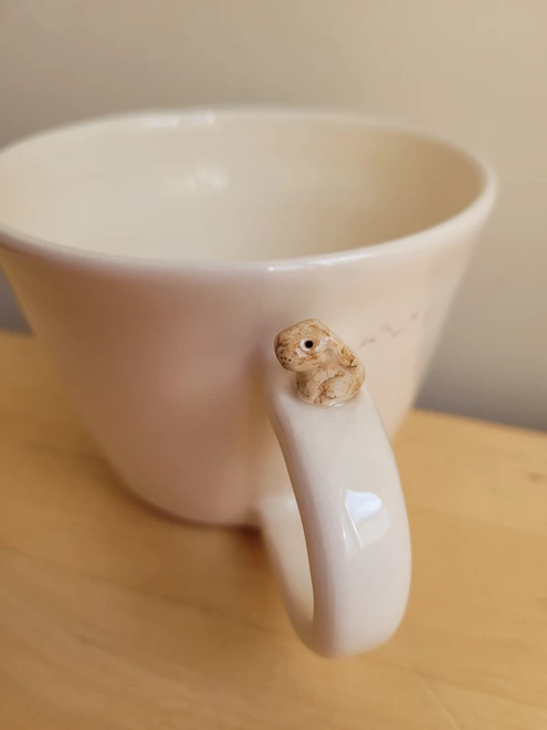 a white pottery bunny cup with a small ceramic rabbit sitting on the top of the handle and tiny pawprints on the cup   