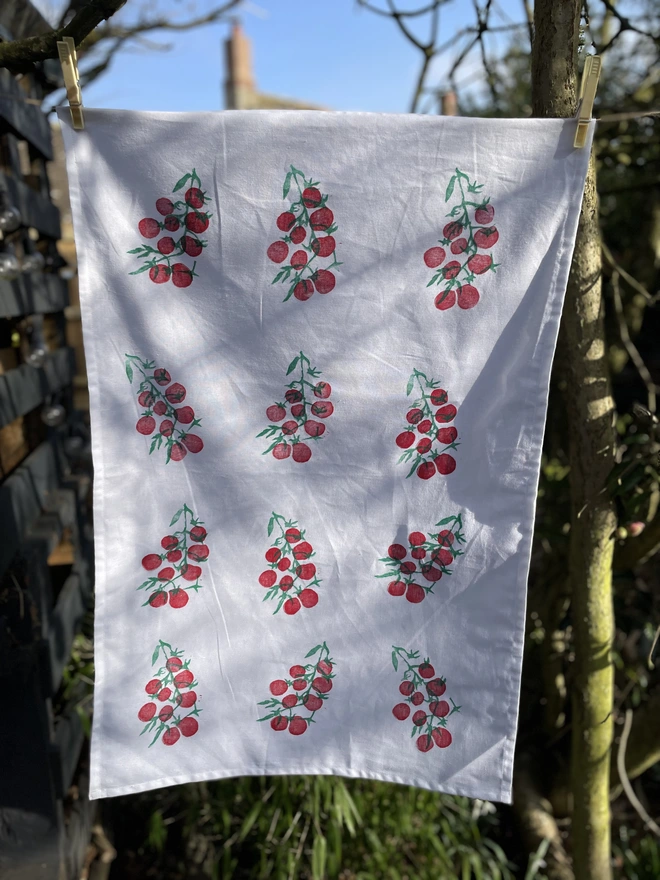 Tomatoes Kitchen Tea Towel. White fabric with a diagonal pattern of red tomatoes hanging in garden