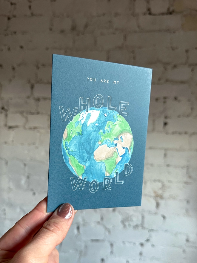 a dark blue greetings card featuring an illustration of Earth with the text “you are my whole world”