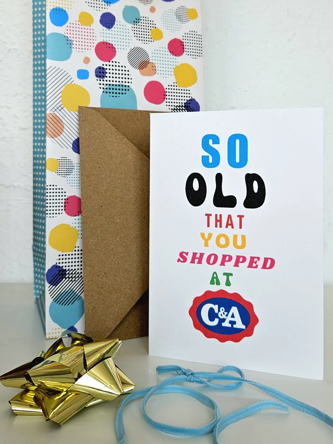 A photograph of the front of a humorous A6 greeting card illustrated using brightly coloured text and the retro shop logo. The text says so old you shopped at C&A