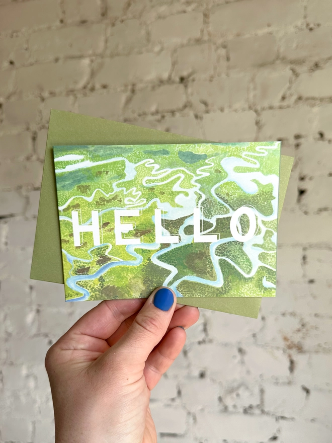 a greetings card featuring an illustration of some of the Everglades landscape with the text “hello” with a green envelope