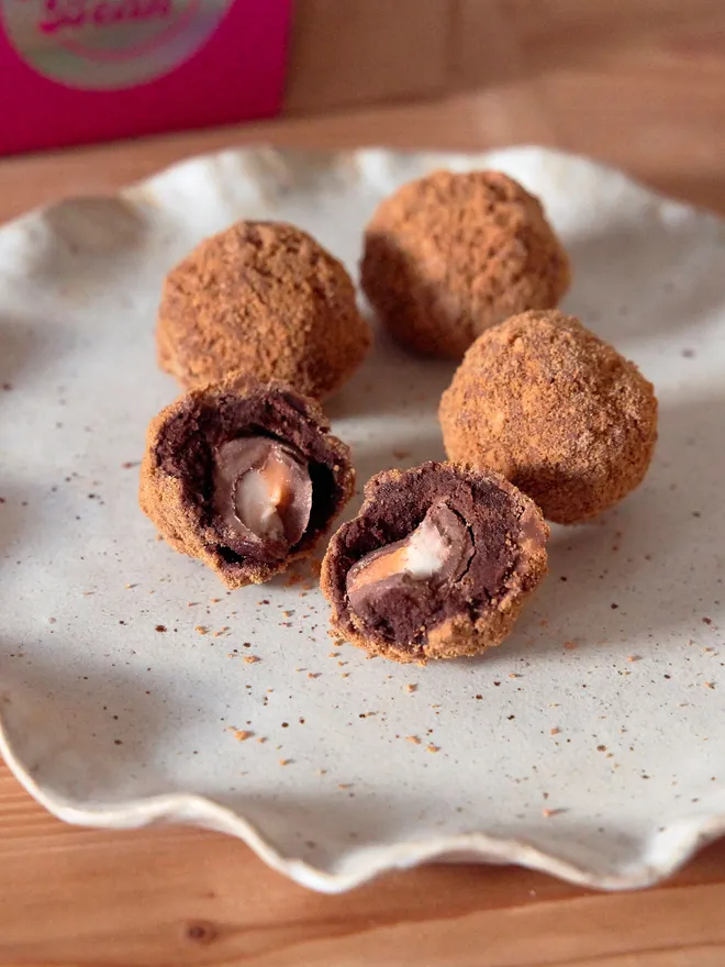 Mini Scotch Egg brownies on a textured speckled plate with one cut open to reveal a creme egg centre, atop a wooden worktop