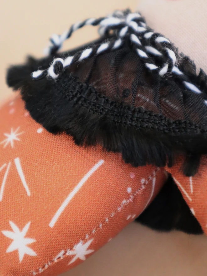 Close up of handmade autumn elf doll with orange patterned top, black ruffled collar with black-and-white twine tie