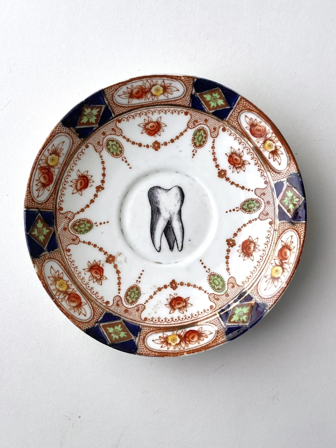 vintage plate with ornate border has a black and white image of a victorian molar tooth in the centre