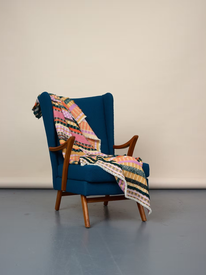 aednat lambswool blanket. a multi coloured patterned blanket, thrown over a blue chair.