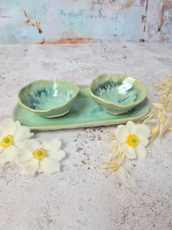 Serveware, Small serving dish crafted from stoneware clay and glazed in Dream Catcher glaze with creams, whites, hints of pink, lilac and specks of metallic gold. Two bowls and an oval dish, tapas dish, snack dish, gift, handmade, homeware, pink background, flowers