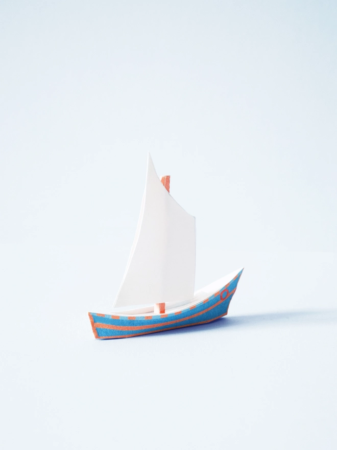 A paper boat with a blue and orange hull and a large sail
